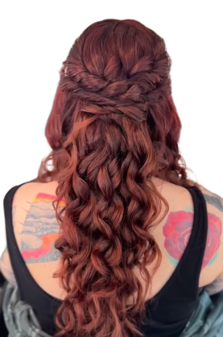 Long, wavy red hair styled with a braid, featuring colorful tattoos on the shoulders.